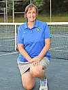 Tennis coach kneeling on court in blue shirt.