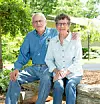 Elderly couple sitting on a log in a garden.