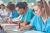 Medical students in scrubs taking notes in a classroom.