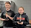 Two children holding trophies in a room.