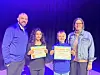 Students holding spelling awards on stage with educators.