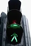 Illuminated green pedestrian signal with a walking figure.