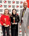 Two students holding trophies with a school official.