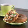 Two colorful donuts and a cup of coffee on a table.