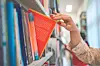 Hand reaching for a red book on a library shelf.