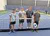 Four boys on a tennis court holding paddles.