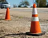 Two orange traffic cones on a gravel roadside.
