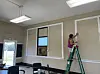 A person painting a wall on a ladder in a community center.