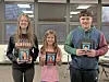 Three students holding awards in a classroom.