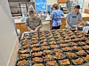 Volunteers preparing meal trays in a kitchen.