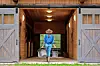 Woman in a hat carrying baskets out of a barn.