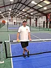 Tennis coach in an indoor facility by the net.