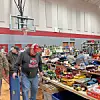 People browsing tables filled with vintage toys in a gymnasium.