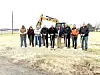 Group of people at a groundbreaking ceremony with shovels and an excavator.
