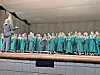Choir in green robes performing on stage.