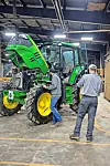 Technicians inspecting a green tractor in a workshop.
