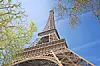 View of the Eiffel Tower from below with trees and blue sky.