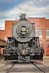 Front view of a vintage steam locomotive at a depot.