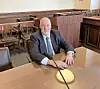 Man seated at a courtroom table with a microphone.
