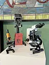 Three vintage microscopes displayed on a pedestal.