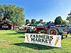 Farmers market with tents and a tractor in a grassy area.