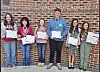 Students holding awards and certificates in front of a brick wall.