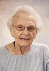 Elderly woman with glasses smiling in a light blue sweater.