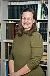 Woman smiling in a library setting with bookshelves behind her.