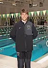 Young swimmer in team jacket poses by the pool.