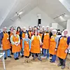 Group of people in orange aprons at a cooking class.