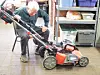 Elderly man inspecting a lawn mower in a workshop.
