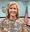 Smiling woman in a floral blouse with an American flag behind her.