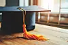 Close-up of a graduation cap with an orange tassel on a wooden surface.