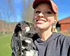 Woman smiling with a goat outdoors in sunny weather.