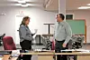 Two people talking in an office with desks and chairs.