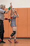 Wrestler celebrating victory with referee in a gym.