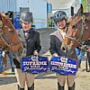 Two riders holding awards next to their horses at a horse show.