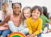 Three smiling children sitting together with a rainbow toy.