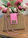 Woven handbag with pink detail on a table with flowers.