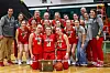 Basketball team celebrating with trophy and medals in a gym.