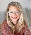 Smiling woman with glasses sitting on a couch.