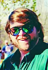 Man smiling in sunglasses at an outdoor event.