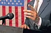 Speaker gesturing at a podium with an American flag behind.