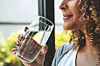 Woman holding a glass of water by a window.