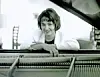 Woman smiling while leaning on a piano.