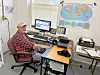 Man at desk with computer and world map behind him.
