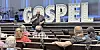 Speaker in front of illuminated 'GOSPEL' letters addressing an audience.