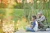 A grandfather and grandson fishing on a dock at sunset.
