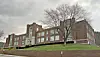 Brick school building on a hillside under gray clouds.
