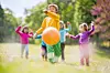 Children playing with a large orange ball in a park.